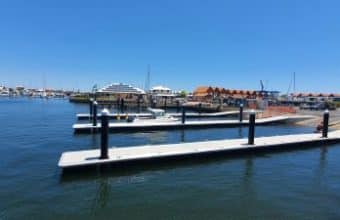 Empty docks and floating pontoons rest on calm water, with boats and buildings silhouetted against a clear blue sky.