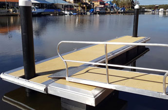 A small dock with a ramp leads to calm waters, surrounded by floating marinas and buildings.